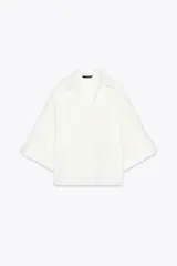 Camisa blanca de cuello solapa con escote pico y manga corta ancha acabada en vuelta con trabilla y botón. Cierre frontal con botones.