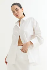 Camisa blanca de corte amplio, con cuello clásico, cierre frontal con botones y mangas largas con puños abotonados.