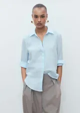 Camisa celeste de lino con cuello camisero, manga larga con puños abotonados y cierre frontal con botones.