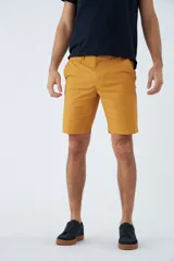 Bermuda de gabardina color mostaza, corte chino, con bolsillos laterales y traseros, cierre con cremallera y botón, trabillas para cinturón y logo bordado.