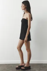 Vestido corto negro sin mangas, con escote palabra de honor y pespuntes marcados. Cierre trasero con cremallera oculta.