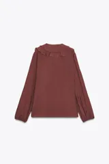 Camisa color crudo confeccionada en tejido con lyocell. Presenta escote en pico, mangas largas abullonadas con elástico en los puños, volantes frontales y cierre frontal con botones.