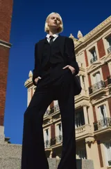 Conjunto de blazer, chaleco y pantalón de vestir de color gris con rayas verticales finas. El blazer es de doble botonadura, el chaleco tiene cuello en V y el pantalón es de corte palazzo.