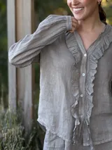 Camisa blanca de lino con cuello mao, mangas largas abullonadas y cierre frontal con botones de nácar. Presenta volados en el frente y puños elásticos.