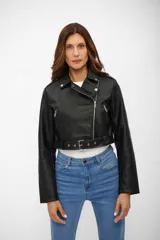 Campera estilo biker corta, color negro, confeccionada en cuerina (poliuretano) con forro de poliéster. Presenta solapas con broches, cierre asimétrico plateado, bolsillos con cierres y un cinturón con hebilla en el ruedo inferior.