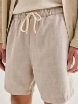 Bermuda de hombre color gris claro, con cintura elástica y cordón ajustable. La tela presenta una textura visible, similar al lino o una mezcla ligera.