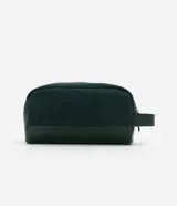Neceser rectangular mediano de terciopelo verde oscuro con textura acanalada, cierre de cremallera dorada y asa lateral de cuero sintético.