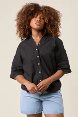 Camisa color beige claro, de corte clásico, con cuello, botones frontales, bolsillo en el pecho y mangas tres cuartos con presilla para sujetar.