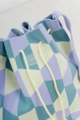 Bolso tipo bucket tejido con diseño geométrico en tonos lila, celeste y amarillo. Tiene cordón ajustable y correa ancha al tono para llevar al hombro o cruzado.