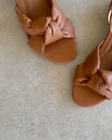 Sandalias bajas color marrón, con tira fina al tobillo y detalle de nudo en el empeine.