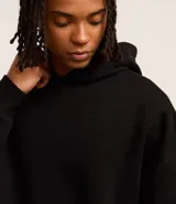 Buzo negro con capucha, manga larga, bolsillo canguro y barras ajustadas. Corte boxy.
