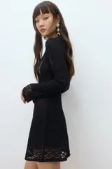 Vestido mini negro de manga larga en tejido de punto suave con escote redondo y falda con leve vuelo. Presenta secciones caladas en mangas, delantero y espalda, y secciones en punto pointelle en puños y bajo.