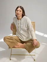 Chomba a rayas horizontales color crudo y gris, con capucha y botones de madera. Tiene cordones de ajuste en la capucha y puños con ribete verde flúor.