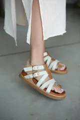 Sandalias de cuero color blanco con tiras cruzadas y hebillas doradas.