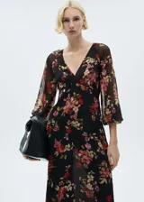 Vestido midi de gasa color negro con estampado floral en tonos rojos, rosados y verdes. Tiene escote en V, mangas largas abullonadas y corte evasé.