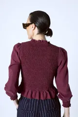 Blusa color borgoña con escote redondo con volados, mangas largas abullonadas y cuerpo fruncido.