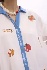 Camisa blanca estampada con dibujos de motivos veraniegos, con cuello clásico y tapeta de botones azul.