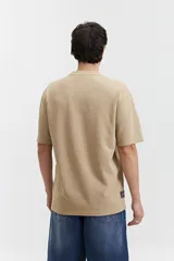 Remera beige de manga corta con textura y corte oversize. Presenta un pequeño bordado en relieve en el pecho.