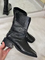 Bota negra de caña media con textura de cocodrilo, punta cuadrada y tacón bajo.