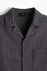 Camisa de manga corta en sirsaca de algodón a rayas grises y negras. Modelo boxy con cuello abierto, tapeta lisa, bolsillo superior y bajo recto. Corte holgado.