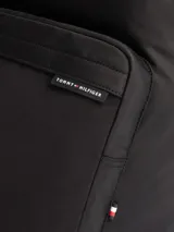 Mochila negra de poliéster con múltiples bolsillos, cierre de doble cremallera, asa superior, correas ajustables y acolchadas, compartimento principal, dos bolsillos interiores abiertos, bolsillo interior con cremallera, bolsillo exterior con cremallera y logo de Tommy Hilfiger en la parte delantera.