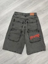 Bermuda de jean gris oscuro con bolsillos delanteros y traseros. Estampado rojo con la palabra "Rockstar" en el bolsillo trasero derecho.