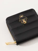 Billetera pequeña de cuero vacuno graneado color negro con diseño matelasseado. Tiene cierre metálico, divisiones internas para tarjetas y forrería de jacquard. Aplique metálico dorado con diseño de mono.
