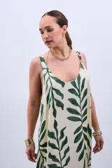 Vestido largo color crudo con estampado de hojas verdes, de corte amplio y breteles finos.