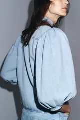 Blusa de denim celeste con cuello solapa y mangas abullonadas por debajo del codo. Cierre frontal con botones.