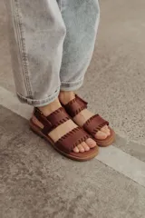 Sandalias de cuero marrón con tiras tejidas a mano y costuras a la vista, con base plana.