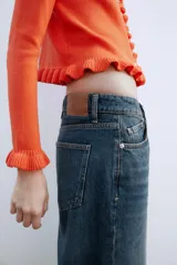 Chaqueta de punto rosa con cuello redondo y manga larga. Detalle de volantes en los bordes y cierre frontal con botones.