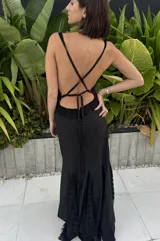 Vestido largo de silueta fluida confeccionado en seda con detalles de encaje. Presenta un diseño negro con estampado de lunares blancos, escote en V profundo y espalda descubierta con tiras cruzadas. La falda cuenta con paneles de encaje que aportan movimiento y delicadeza.