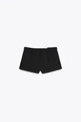 Shorts negros de tiro medio con cintura con trabillas y pliegues delanteros. Cierre frontal con cremallera, botón y ganchos metálicos.