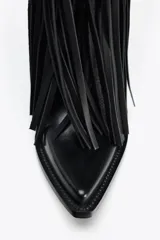 Bota de cuero negra estilo cowboy, con punta fina, taco de 7,5 cm y detalle de flecos en el cuerpo.