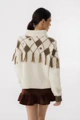 Sweater tejido de punto color crudo con cuello alto y diseño de rombos marrones con flecos.