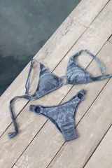 Conjunto de bikini turquesa con textura acanalada, compuesto por un corpiño triangular con argolla central y una bombacha vedetina con argollas en los laterales.