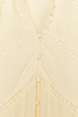 Blusa color crema de escote pico con volantes y manga larga. Detalle de jaretas y entredoses a tono. Cierre frontal con botones forrados a tono.