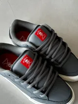 Championes CIRCA modelo AL 50 PRO, color gris con detalles en negro y rojo. Fabricados con materiales de alta calidad, puntera triple cosida, lengüeta acolchada con parche con el logo y ojales metálicos.