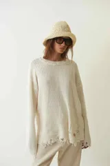 Sweater tejido color crudo, de manga larga con efecto desgastado y deshilachado en el ruedo y puños. Tiene cuello redondo y calce holgado.