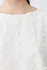 Blusa color beige con textura de lunares en relieve, cuello redondo y mangas cortas.