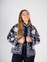 Chaqueta corta negra con bordado floral blanco, cuello camisero y mangas largas.
