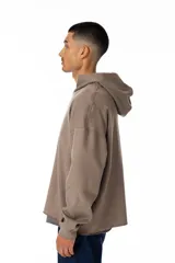 Buzo con capucha color marrón topo, de corte oversize y terminación sin franja en la cintura. Presenta un estampado pequeño en el pecho con el logo de la marca en color lila.