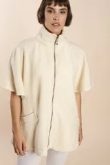 Capa acampanada color beige con manga corta, cierre metálico a la vista, cuello recto, bolsillos con tapa y terminaciones envivadas. Confeccionada en lana fina sin teñir, diseñada exclusivamente por Don Baez.