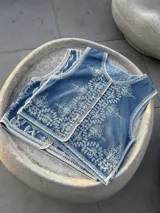 Chaleco de jean celeste con bordado de flores blancas y botones de madera.