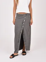 Falda larga de denim color gris oscuro, con diseño cruzado frontal (wrap) que se ajusta con botones plateados, creando una abertura pronunciada.