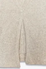 Camiseta color beige de tejido de punto, con cuello halter y escote pico. Tiene cierre frontal con botones y mangas cortas.