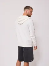 Canguro blanco con cierre frontal, capucha con cordones ajustables y logo de la marca bordado en el pecho.