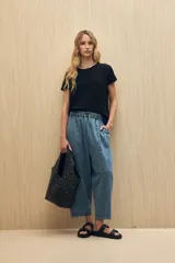 Remera de manga corta color gris claro, confeccionada en algodón con textura liviana y suave al tacto. Presenta costuras decorativas en los laterales y mangas con pequeño doblez.