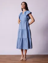 Vestido midi celeste de tencel con cuello a la base y escote en V. Cintura con frunces y lazo de ajuste. Terminación de ruedo con volado.