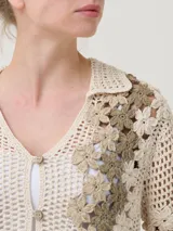 Sweater tejido a crochet color crema con flores bordadas en tonos beige y marrón. Tiene cuello camisero, mangas cortas y cierre frontal con botones.